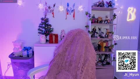 Media: A video of a cozy, Christmas-themed room with a fluffy blanket draped over a chair, a decorated tree, a red gift box, and a bookshelf filled with figurines and ornaments.