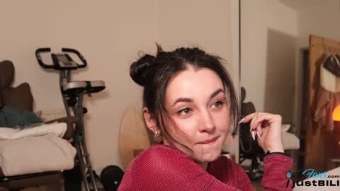 Media: A video of a young woman with dark hair in buns, wearing a red sweater, smoking, in a gym setting with exercise equipment and a mirror.