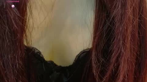 Media: A close-up video of a woman's neck and chest, showcasing her long, reddish-brown hair with black lace bralette peeking out. The background is blurred, focusing on the texture of her hair and the delicate lace.