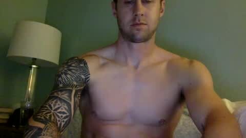 Media: Video of a shirtless, fit white man with a short beard, showcasing a detailed black and gray tattoo sleeve on his right arm, in a dimly lit room with a green wall and a lamp with a white shade.