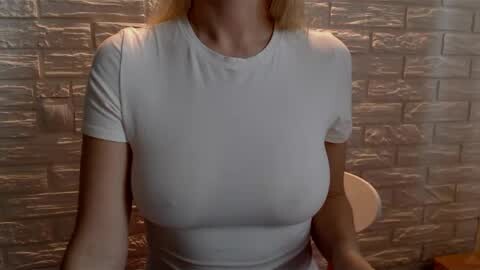 Media: Video of a woman wearing a snug, white, short-sleeved t-shirt, highlighting her large breasts and narrow shoulders against a textured, grey brick wall background.