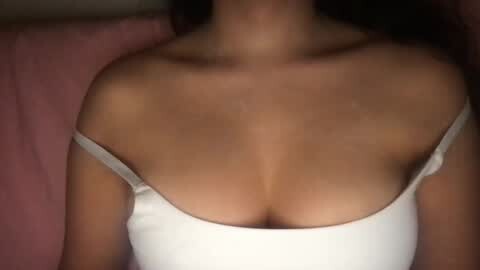 Media: A video of a woman's cleavage, showcasing medium-sized breasts in a white off-shoulder top, against a pink background. Her skin tone is light, and her dark hair is visible at the top.