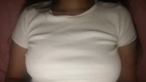 Media: Video of a pregnant woman with medium brown skin wearing a tight, white, short-sleeved shirt, lying on a pink bed. Her belly is prominent, and her face is not visible.