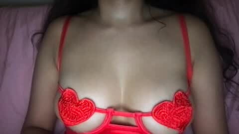 Media: Video of a light-skinned woman with long dark hair, wearing a red lace bra with heart-shaped cutouts, lying on a pink bedspread.