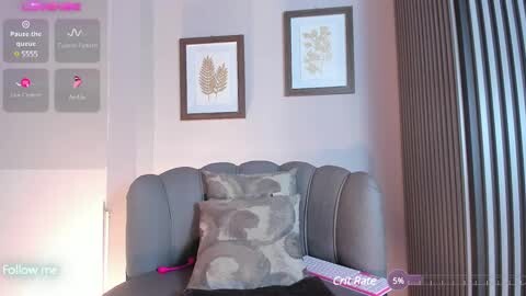 Media: A video of a modern living room featuring a gray sectional sofa with a camo-patterned throw pillow. Artwork with wheat and floral designs hangs on the light gray wall. A virtual camera overlay displays \"Follow\" and \"Play\" options.
