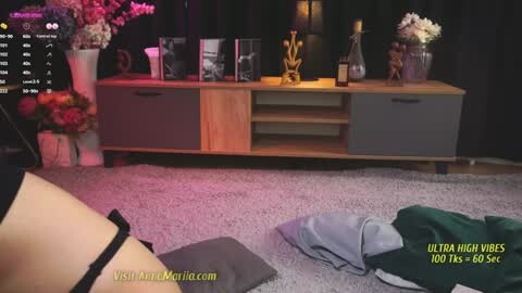 Media: Video of a woman lying on a carpeted floor, wearing black lingerie, with a wooden sideboard behind her.