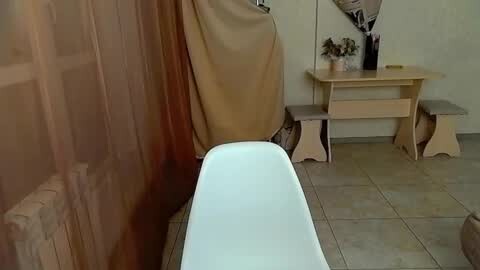 Media: Video of a beige-tiled bathroom with a white bathtub partially covered by a beige cloth, a wooden vanity table with potted plants, and a stool.