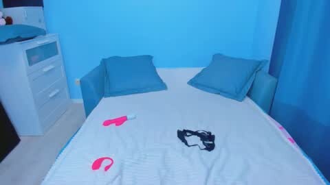 Media: Video of a small, neatly arranged bedroom with light blue walls, white dresser, and a single bed covered in a white quilt with pink and black heart-shaped pillows.