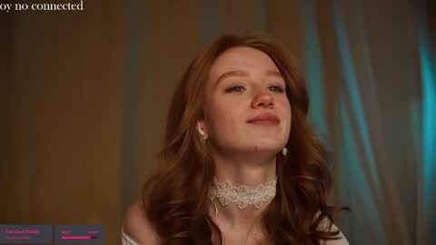 Media: Video of a young woman with long, wavy red hair, wearing a white lace choker and off-shoulder top, set against a blurred, muted background.