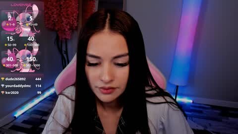 Media: Video of a young woman with long black hair, closed eyes, in a cozy, dimly lit room with a pink gaming chair, blue and purple ambient lighting, and a digital clock displaying \"2:20.\
