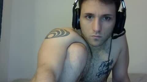 Media: Video of a shirtless, muscular man with short brown hair wearing black headphones, showing a large tribal tattoo on his right shoulder and a black text tattoo on his chest.