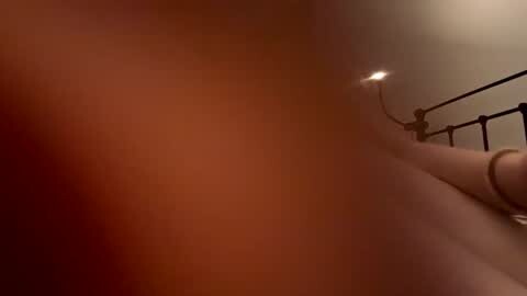 Media: Video of a dimly lit bedroom with a beige wall and a dark wooden bed frame on the right side. The bed is slightly out of focus, creating a hazy, almost dreamlike atmosphere.