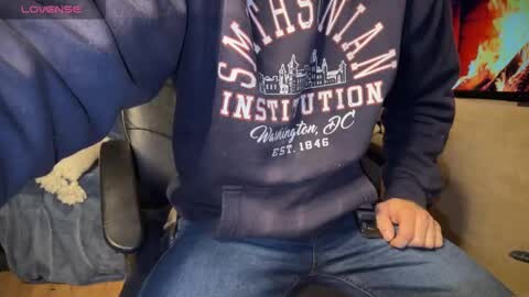 Media: Video of a person wearing a \"Smithsonian Institution\" sweatshirt and jeans, sitting on a black chair in a room with a TV displaying colorful images.