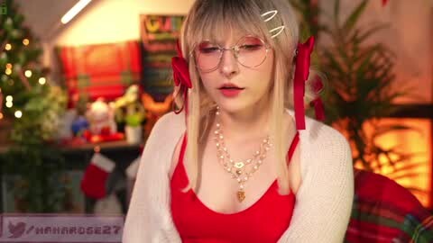 Media: A video of a young woman with platinum blonde hair, wearing glasses, a red top, and a white cardigan, adorned with red ribbons, in a festive, warmly lit room with Christmas decorations and a fireplace.