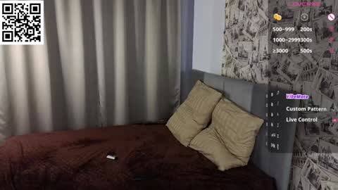 Media: A video of a modern bedroom with a grey headboard, beige pillows, and dark brown bedding. The background features a grey wall with a monochrome cityscape mural. A QR code and \"Live Control\" interface overlay the image.