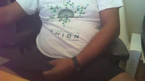 Media: Video of a pregnant woman with dark skin, wearing a white t-shirt with a geometric design and \"NAMIBIA\" text, sitting on a black chair, resting her hands on her belly.