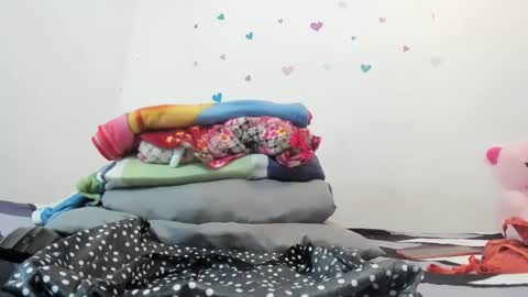 Media: Video of a messy bed with colorful blankets and pillows. The background features heart-shaped decals on a white wall.