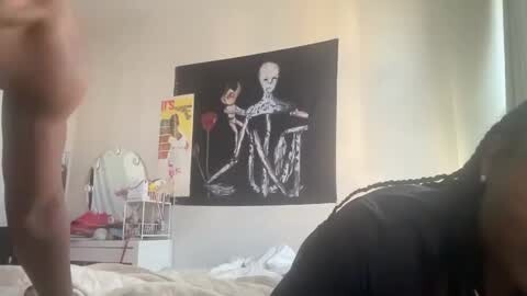 Media: Video of a dimly lit bedroom featuring a large black and white skull print, a cluttered white dresser, and a person in a dark shirt lying on the bed.