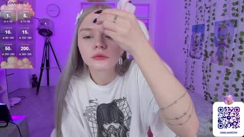 Media: Video of a young woman with long blonde hair, wearing a white T-shirt with a graphic design, sitting indoors. Background features purple lighting, a studio backdrop, and a QR code in the lower right corner.