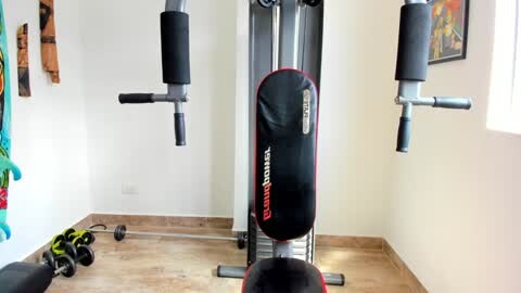 Video of a home gym with a black and red Bowflex SelectTech 552 resistance machine, a black exercise bench, and free weights on a wooden floor.
