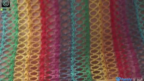 Media: A close-up video of a vibrant, colorful, knitted fabric with alternating stripes in red, yellow, green, and blue, showcasing intricate, interlocking loops. The texture appears coarse and slightly fuzzy.