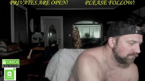 Media: Video of a shirtless, bearded man in a baseball cap, sitting in a dimly-lit room with a Christmas tree, a piano, and a \"Private\" sign.