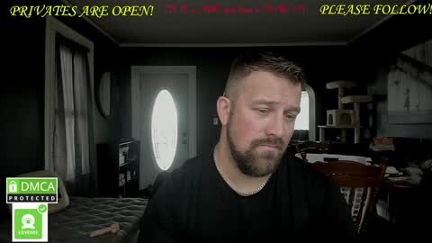 Media: Video of a bearded, middle-aged man with short brown hair in a dimly lit, cluttered room. He wears a black shirt, looks downcast, and a text overlay reads, \"Private are open!\