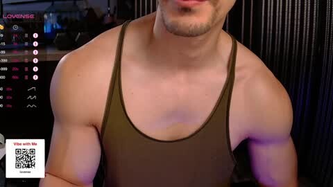 Media: Video of a muscular, light-skinned man with a trimmed beard and short hair, wearing a dark green tank top, taken indoors with a dark, vertical background.