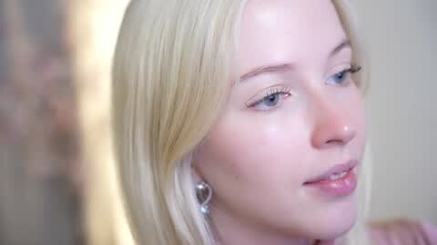 Media: Video of a close-up of a fair-skinned woman with long, straight blonde hair, wearing silver hoop earrings. She has blue eyes and a neutral expression, with soft lighting highlighting her smooth skin.