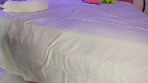 Media: Video of a neatly made bed with white sheets, a plush white pillow, and a colorful stuffed toy in the corner, set against a softly lit background.