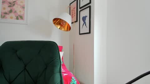 Media: Video of a minimalist bedroom corner featuring a green velvet chair, a white lamp, and framed fish and flower art on white walls.