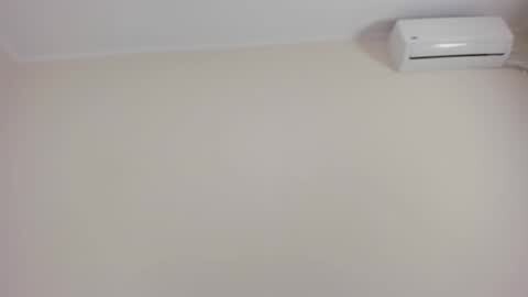Media: A video of a plain, off-white wall with a small, white air conditioning unit mounted near the top right corner. The background is minimal, with no additional objects or decorations.