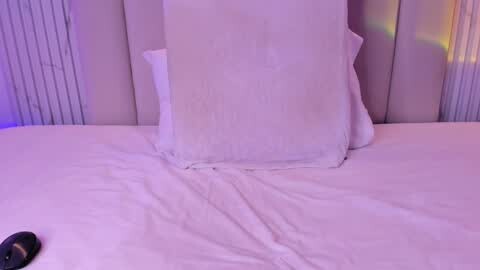 Media: A video of a neatly made bed with white linens and pillows, featuring a large rectangular pillow with a slight indentation. A black remote control is partially visible on the left side of the bed.