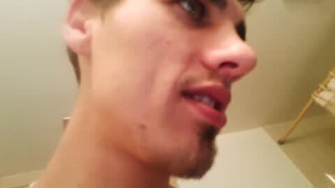 Media: Video of a young man with short brown hair, fair skin, and a light beard, slightly out of focus, looking sideways. Background shows beige walls and a metallic object in the right corner.