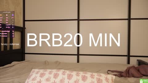Media: Video of a minimalist bedroom with a BBR20 MIN label on the wall, showcasing a bed with beige sheets and floral pillows, a black dresser, and a digital clock.