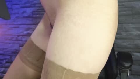 Media: Video of a woman's bare thighs and lower abdomen, wearing beige thigh-high stockings, against a grey stone wall background.