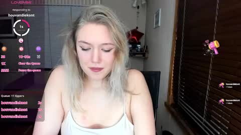Media: Video of a blonde woman in a white tank top, seated indoors, with video game chat overlay.