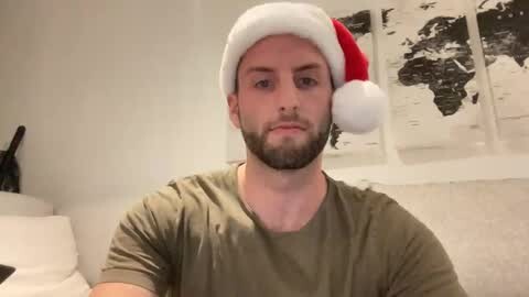 Media: Video of a bearded, fair-skinned man wearing a Santa hat, olive-green shirt, indoors, with white walls and a black-and-white world map on the wall.