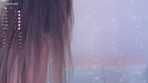 Media: Video of a woman with long, straight brown hair, partially visible in profile. The background is a soft, blurred pastel gradient with scattered white dots. Text on the left lists \"Lovense Lush.\