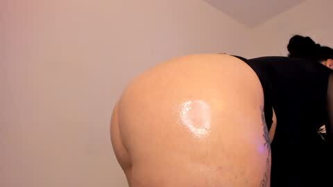 Media: Video of a person with light skin, wearing a tight black outfit, bent over, showcasing their large, shiny, round buttocks.