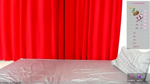 Media: A video of a neatly made bed with a grey duvet and pillow, surrounded by vibrant red curtains, with a digital clock displaying \"LOUNGE\" on the right wall.
