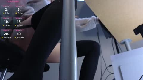 Media: Video of a person wearing black leggings and a gray sweater, sitting on a chair in a dimly lit room with a computer monitor displaying fitness app stats.