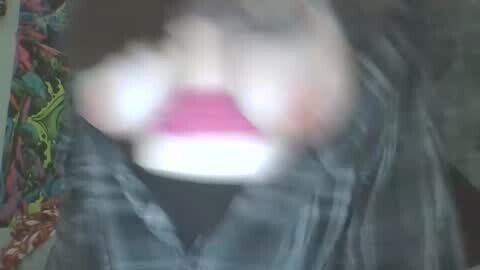 Media: A blurred, low-resolution video showing a person wearing a pink shirt and plaid jacket, with a colorful, patterned blanket in the background.