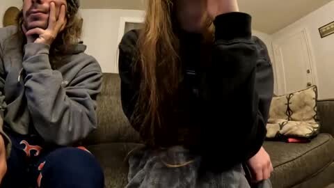 Media: A video of a young woman in a black jacket hugging a crying, middle-aged man with glasses and gray hair, seated on a gray couch in a cluttered living room.
