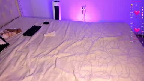 Media: Video of a dimly lit bedroom with a neatly made bed, a black remote control, a white tissue box, and a tall white speaker emitting purple light.