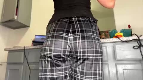 Media: Video of a person's lower back and buttocks, wearing black pants with a white plaid pattern. The background features a kitchen with light gray cabinets, a microwave, and a countertop with various items.
