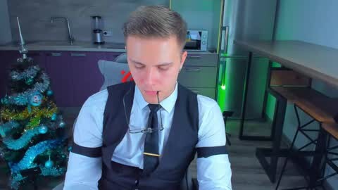 Media: Video of a young, fit man in a white shirt and black vest, blindfolded and gagged, kneeling in a modern kitchen with a Christmas tree and stainless steel appliances.
