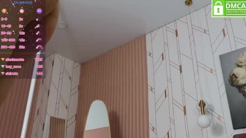 Media: Video of a retro-style bedroom with vertical, light pink striped wallpaper, a white bed, and a wall-mounted sconce. A computer screen in the corner displays chat logs with usernames.