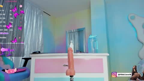 Media: A virtual reality image featuring a pink, lifelike dildo standing upright in a pastel-colored, whimsical bedroom with a calendar, pink decorations, and a woman's silhouette in the corner.