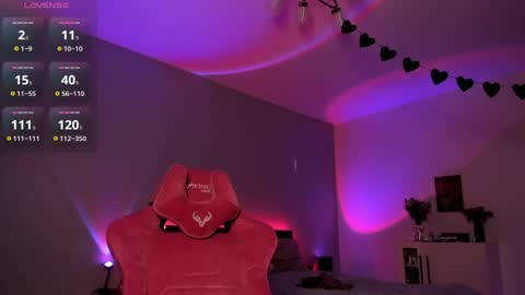 Media: Video of a dimly lit, purple-hued bedroom with a red gaming chair, black heart garland, and a digital screen displaying game stats.